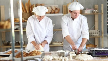 Skilled two baker in apron, adult female and young guy kneading dough, cutting and weighing portioned pieces on floured surface before baking in kitchen