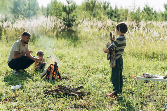 Father camping with children near campfire on grass in forest