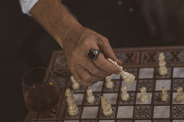 an elderly man plays chess, with a ring on his hands, with a cigar and cognac, checkmates