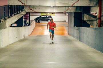 Young fit runner running towards camera in underground garage.