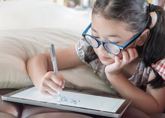 School child girl kid using internet online learning on mobile tablet reading looking at digital...