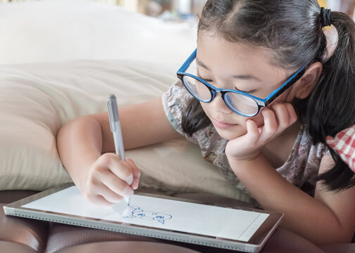 School child girl kid using internet online learning on mobile tablet reading looking at digital screen for educational study for Children’s Eye Health and Safety Month and Blue Light Awareness Day