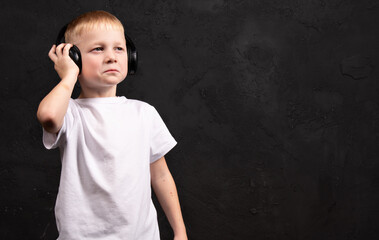 A boy in a white tank top wearing headphones on a black background. Boy listening to music and dancing