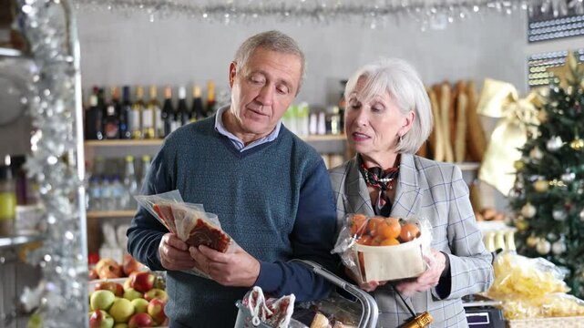 Elderly married couple is looking at sweets in store. Market visitors choose from several deserts, consider nougat, panellets, marzipan. Customers choose national European sweet desserts in sales area