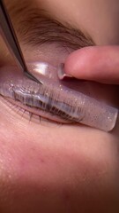 Close-up of a human eye with long eyelashes. The eye has a light iris, possibly green or blue. The eyelashes are thick and curved due to the lamination procedure, giving the eye a expressive and well-