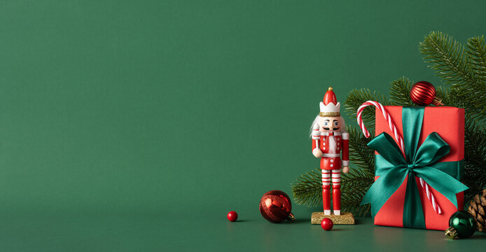 A charming Christmas scene featuring a nutcracker and a wrapped gift box with green ribbon against a green background. Perfect holiday decoration theme with baubles and fir branches