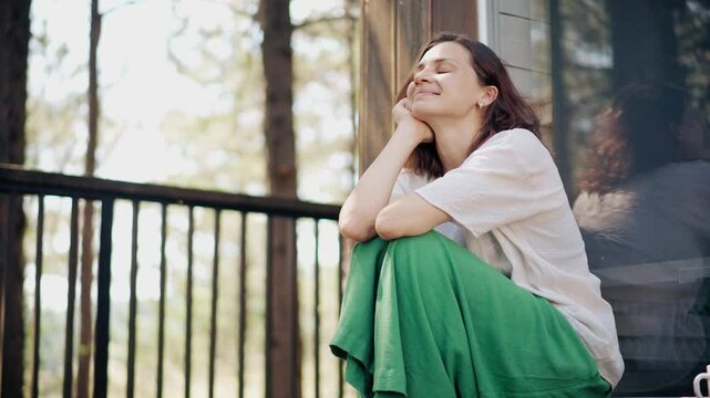 A young Caucasian woman relaxing while sitting on the veranda of a wooden country house in the woods