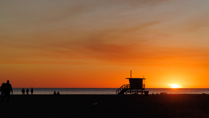 Los Angeles beach at sunset, featuring a lifeguard tower silhouette against a glowing orange and purple horizon