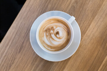 A white cup of cappuccino with velvety foam. The hot drink, adorned with an elegant milk art pattern, highlights the barista's skill.