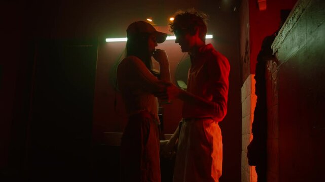 Romantic couple hiding from friends in bathroom in club, girl exhaling vapour through mouth and her boyfriend inhaling it