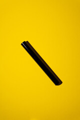 Close-up of empty black mascara and brush mockup on bright yellow background. Striking contrast of bold beauty and floral freshness, perfect for makeup, cosmetics