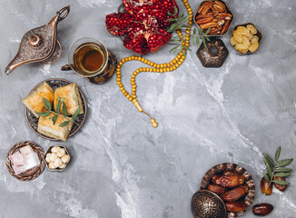 Fototapeta premium Stylish banner with traditional Arabic tableware and food sets, cup of tea, Koran and rosary on gray stone background. Ramadan table top view