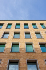 Close-up view of a modern building facade with symmetrical brickwork and multiple windows, showcasing urban architecture and design. Empty space for text.