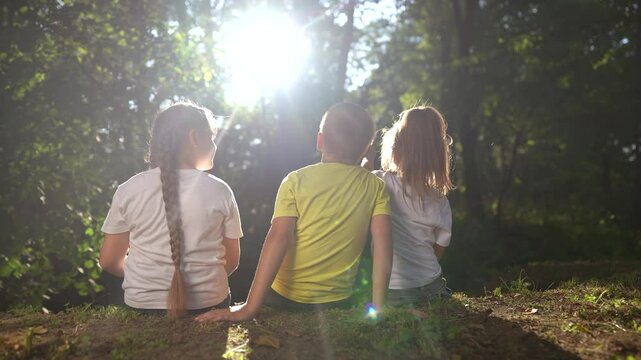children sit on the banks of the river. happy family childhood dream concept. a group of little children sit together by the river and talk. lifestyle kids spend time outdoors in nature in the forest