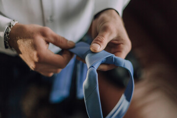 A man is holding a blue tie and is adjusting it. Concept of formality and attention to detail, as the man is carefully adjusting the tie to ensure it is properly aligned