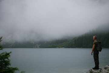 Man on the Shore of Mountain Lake in Misty Pine Forest