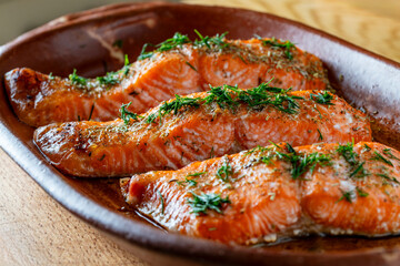 Oven roasted salmon fillets sprinkled with fresh green herbs and spices in a baking dish, closeup. Healthy food diet