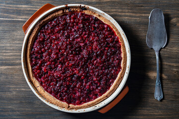 Delicious autumn pie on shortcrust pastry with cranberries on a wooden table with a cake spoon. Cranberry cake with jam and sugar in a baking dish, rustic style, closeup, top view