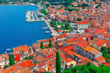 Aerial view of Rovinj, a picturesque coastal town in Croatia. Dense cluster of terracotta-roofed buildings, narrow streets, and a prominent waterfront lined with boats and yachts