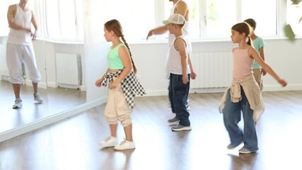 Happy young girl and boy in casual clothes performing hip hop dance in modern dancing room during training with male teacher 