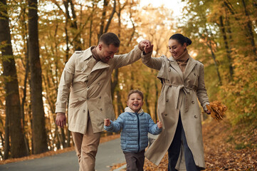 Running, having fun. Happy family are together in the autumn forest near the road