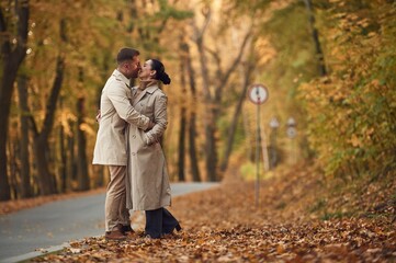 Kissing each other. Lovely couple are together in the autumn forest near the road