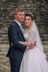 A bride and groom are posing for a picture. The bride is wearing a white dress and the groom is...