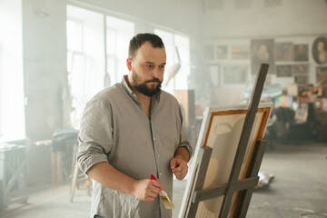 Male artist painting on canvas in a sunlit art studio