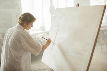 A young female artist working with acrylics on a canvas in a sunlit art studio.