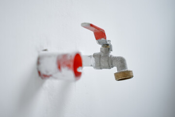 Naklejka premium Close-up of water faucet with red handle protruding from white wall in empty apartment. Plumbing work during home renovation