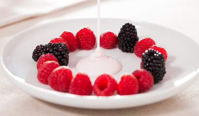 Fresh raspberries and blackberries laid out on a white plate in circle with yogurt