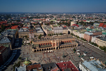 Aerial view of Krakow main market square with historic Cloth Hall (Sukiennice) surrounding colorful buildings on sunny day. Cityscape of Krakow in Poland with tourists walking in old town