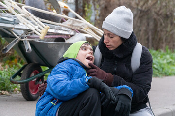 woman with son sitting on curb in black jacket, poverty, poor people collecting scrap metal, wheelbarrow, garbage collection, Europe, America, USA, Russia, unhappy woman with child, alcoholism