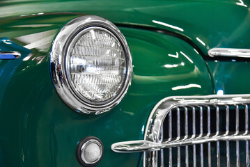 Round headlight on a green retro car. Fragment of car detail.