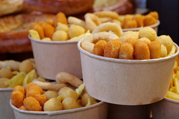 Fried potatoes, cheese fried balls and other baked goods in large paper bowls