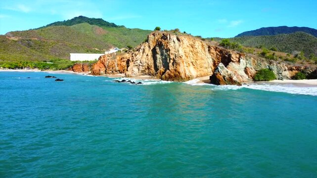 A rocky shoreline with a lighthouse in the distance. The water is calm and the sky is clear
