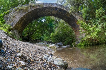 Historic stone bridge Pont du Bucatoghju in Corsica surrounded by lush greenery and natural beauty