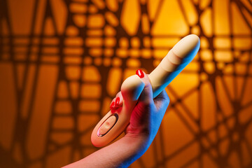 A gentle womans hand with seductive red nails grips a yellow clitoral vibrator tightly in a fist. 
