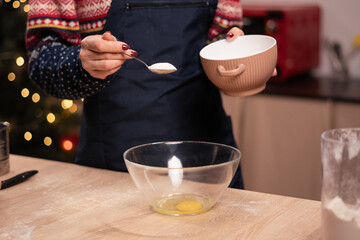 Woman in apron preparing the dough, bake cookies on the Christmas kitchen, adding sugar to eggs on the table