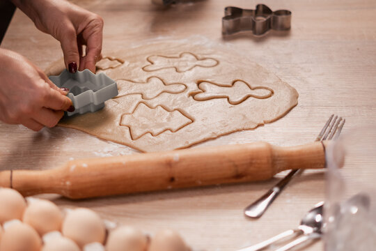 Close-up of female hands making cookies from brown raw dough for baking traditional Christmas gingerbread using cutters in the shape of Christmas tree, on a wooden table. Sweet treat