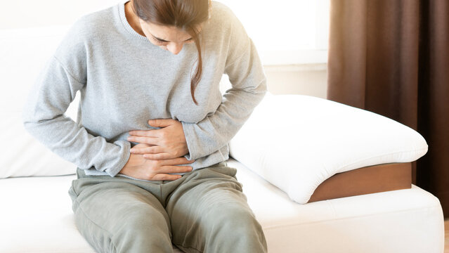 Young woman sitting on a sofa, holding her belly with a painful expression