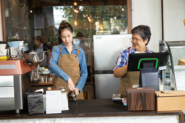 Asian mother and daughter bonding relationship small business lifestyle open cafe coffee shop after retirement, happy 60s elderly senior female laughing with young barista waitress learning technology