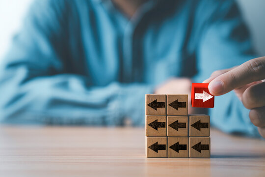 Businessman holding white right arrow on red wooden block move in different direction with black arrow for business and technology disruption concept.