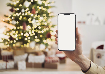 Phone mockup in hand in christmas interior with christmas tree, stars, gifts and decoration, Mobile phone with blank white phone screen, Winter holiday online shopping and advertisement concept