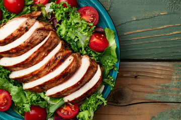 Grilled chicken breast ( fillet ) with lattuce salad and cherry tomatoes . Top view