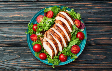 Grilled chicken breast ( fillet ) with lattuce salad and cherry tomatoes . Top view
