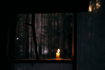 a burning candle stands at the window of the hut overlooking the dark forest. The atmosphere of comfort and solitude in the winter forest