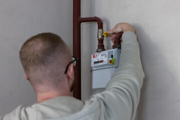 Man turns off yellow gas tap on the gas meter. Rear view. Closeup, selective focus.