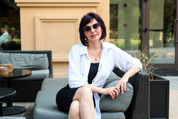 Portrait of an elegant woman 40-44 years old sitting on a comfortable sofa in a city cafe.