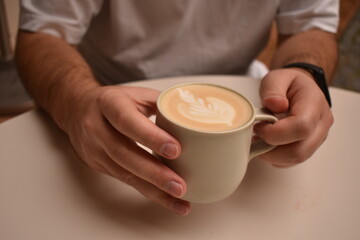 Man holding a cup of hot, aromatic cappuccino — a cozy coffee break full of warmth and calm.